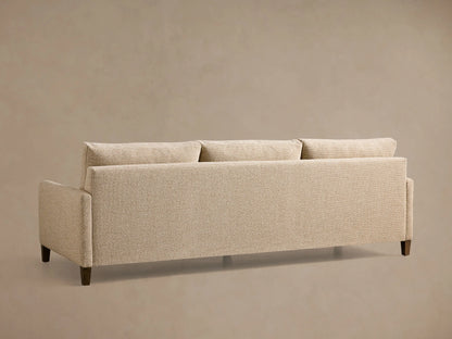 Rear view of a beige textured Kipton Slim Arm Elevated Three-Cushion Sofa with three back cushions and elevated mocha finish feet.