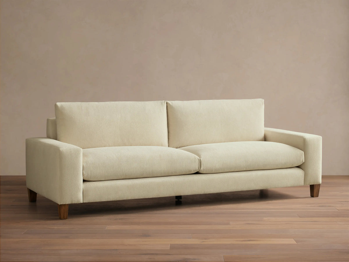 Front view of a cream Kipton Wide Arm Elevated Sofa with wide square arms, two back cushions, two seat cushions, and elevated mocha-finished legs.