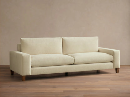 Front view of a cream Kipton Wide Arm Elevated Sofa with wide square arms, two back cushions, two seat cushions, and elevated mocha-finished legs.