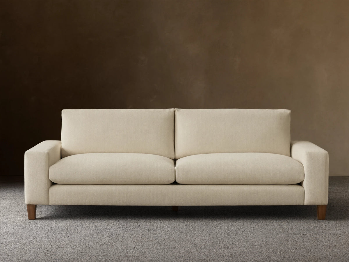 Front view of a cream Kipton Wide Arm Elevated Sofa with wide square arms, two back cushions, two seat cushions, and elevated mocha-finished legs.
