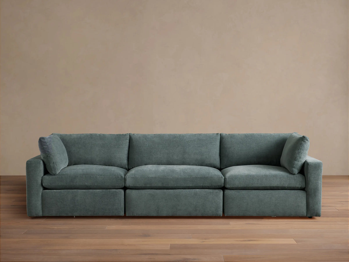 Beale Three-Piece Modular Sofa in muted blue-green fabric, plush cushions, against a light wall on a wood floor.