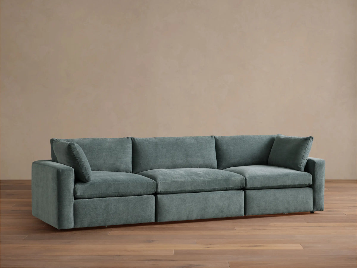 Beale Three-Piece Modular Sofa in muted blue-green fabric, plush cushions, against a light wall on a wood floor.