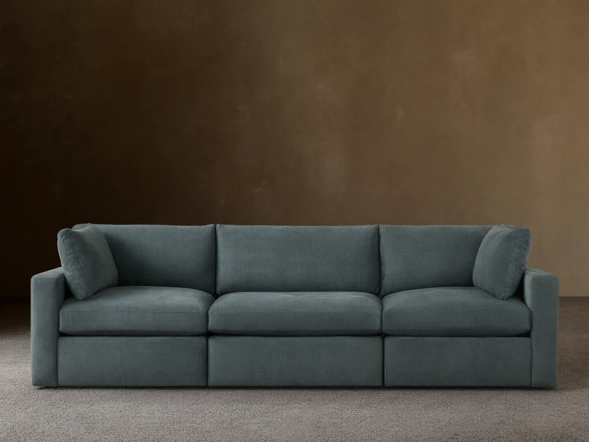 Beale Three-Piece Modular Sofa in muted blue-green fabric, plush cushions, against a light wall on a wood floor.