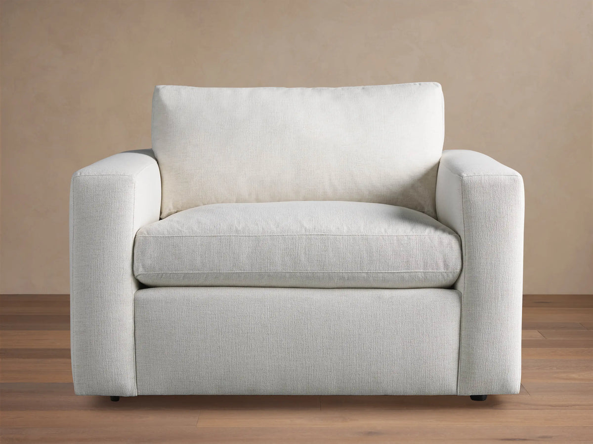 Beale Chair, a modern off-white fabric armchair with wide, square arms and soft cushions, on a wood floor against a beige wall.