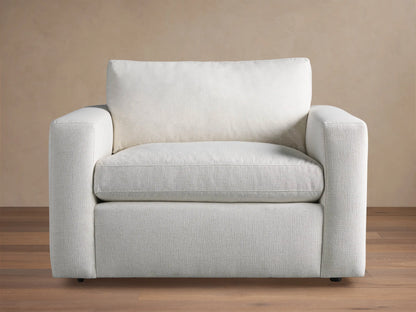 Beale Chair, a modern off-white fabric armchair with wide, square arms and soft cushions, on a wood floor against a beige wall.