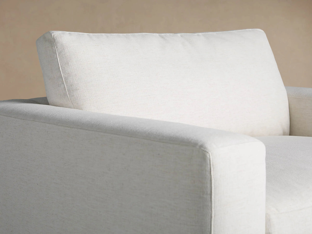 Plush off-white upholstered Beale Chair, front view, with wide arms & soft cushions, on wooden floor against a tan wall.
