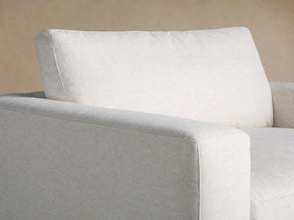 Plush off-white upholstered Beale Chair, front view, with wide arms & soft cushions, on wooden floor against a tan wall.