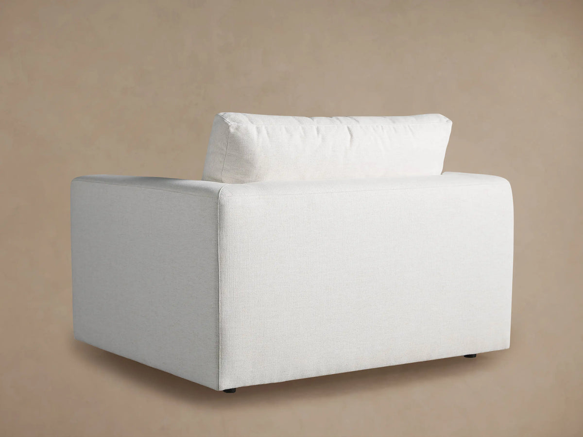 Angled close-up of Beale Chair's light cream textured fabric armrest and plush back cushion.