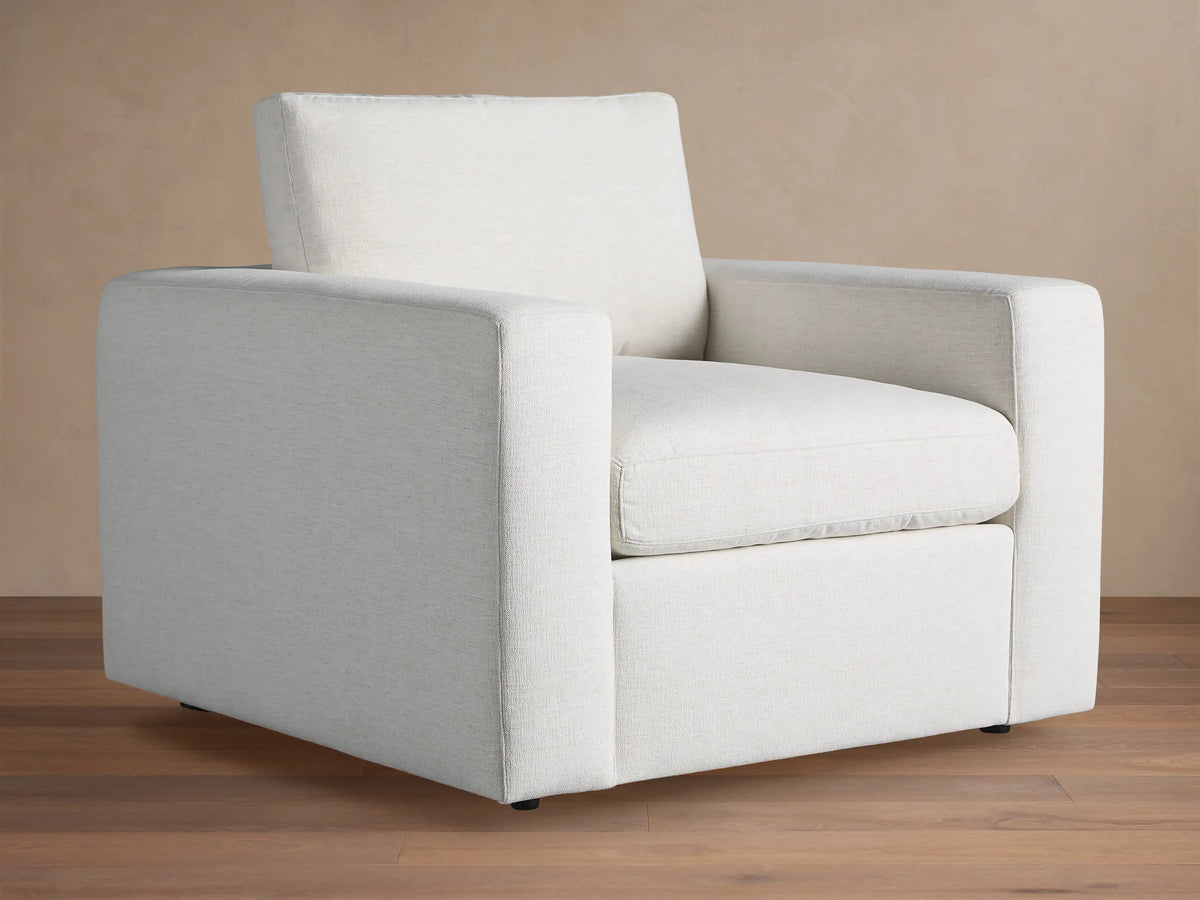 Beale Chair: a modern, off-white, boxy armchair with wide arms and textured fabric, angled on a wooden floor.