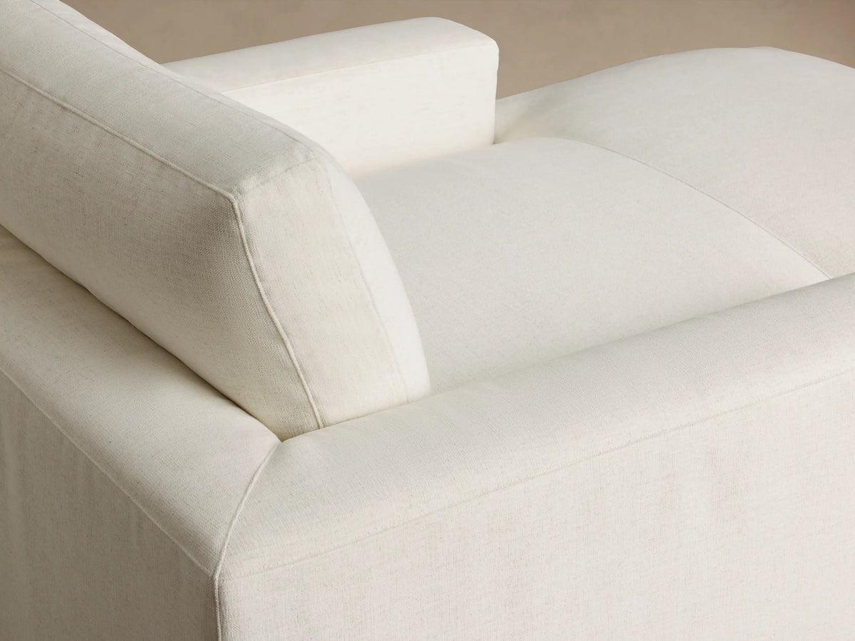 Front view of cream-colored chaise lounge with wide arms and soft textured upholstery.