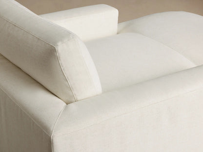 Front view of cream-colored chaise lounge with wide arms and soft textured upholstery.