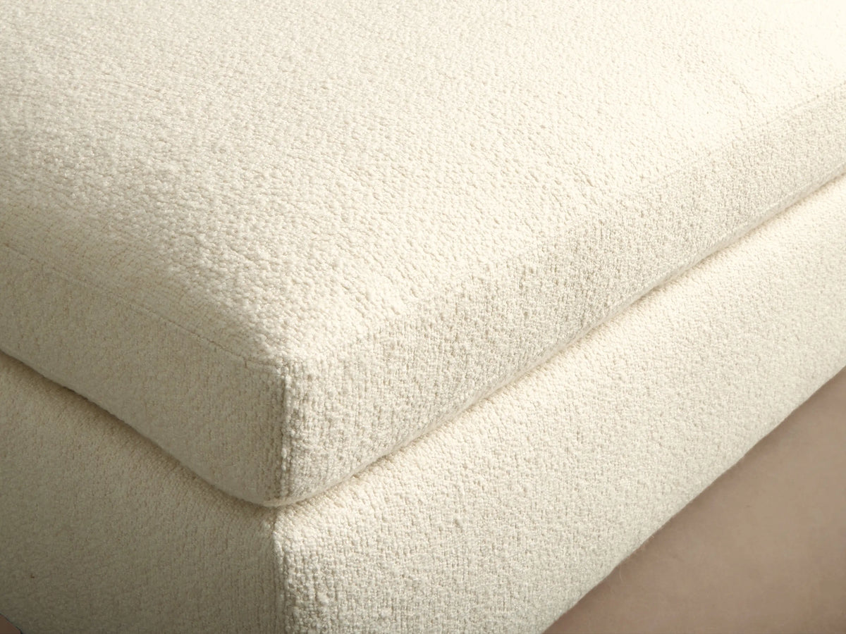 Beale Ottoman, off-white textured fabric, rectangular with a soft, rounded top cushion, on a dark wood floor.