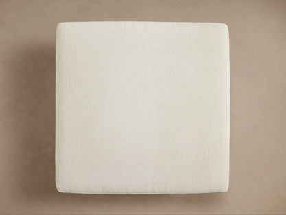 Interior view of an open cream upholstered storage ottoman, revealing a folded brown and cream plaid throw blanket with fringe inside.