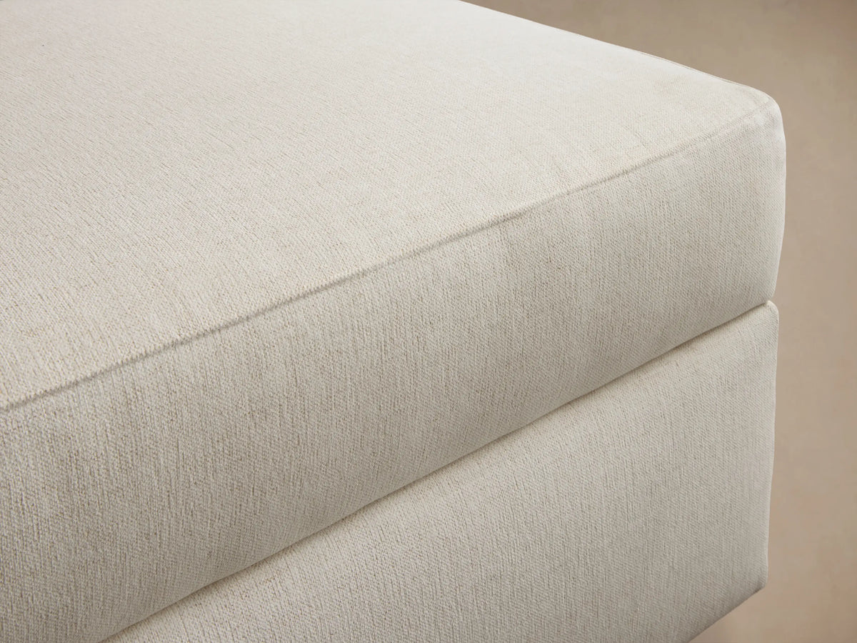 Front view of a light beige rectangular ottoman with a plush, upholstered cushion top.