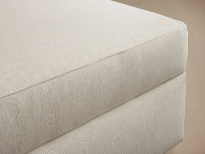 Front view of a light beige rectangular ottoman with a plush, upholstered cushion top.