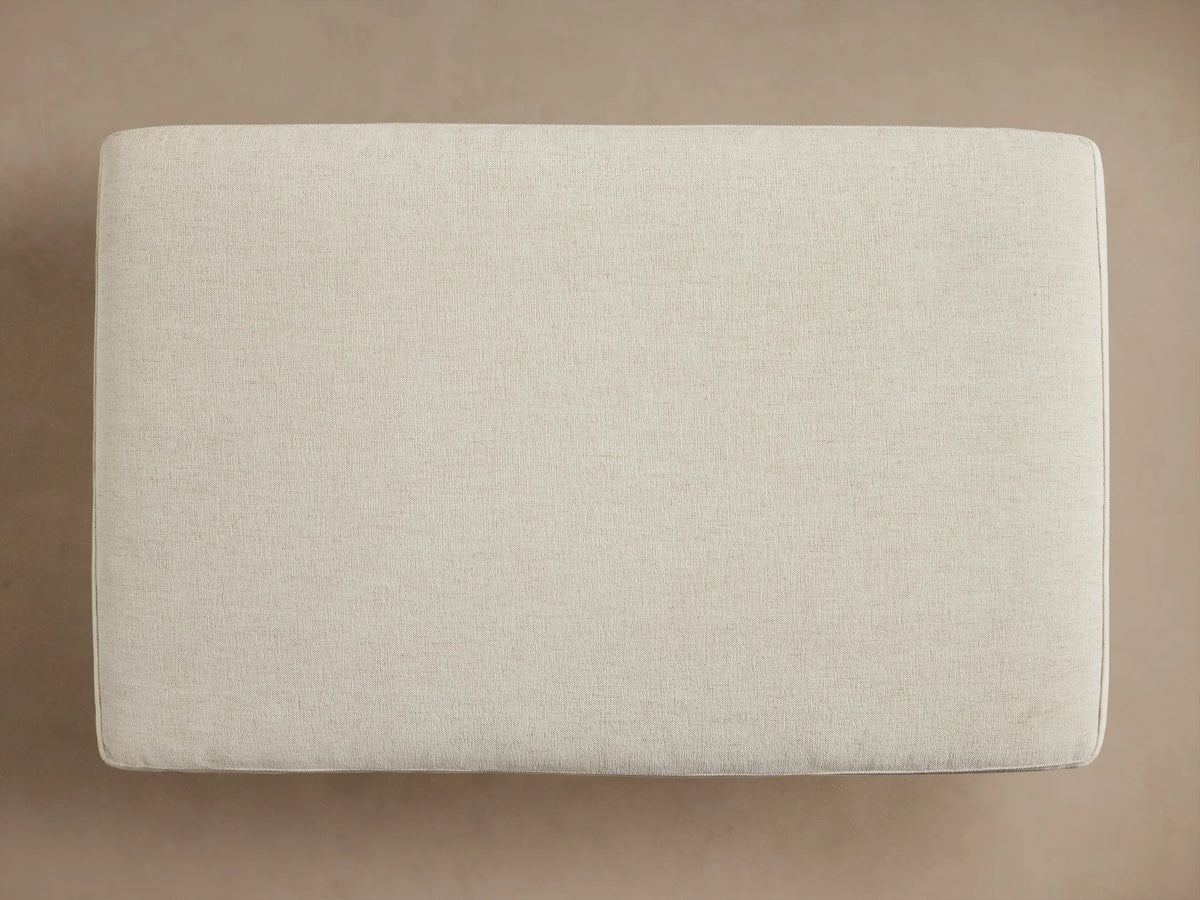 Interior view of an open cream storage ottoman, filled with a folded ribbed taupe blanket and a textured brown throw.
