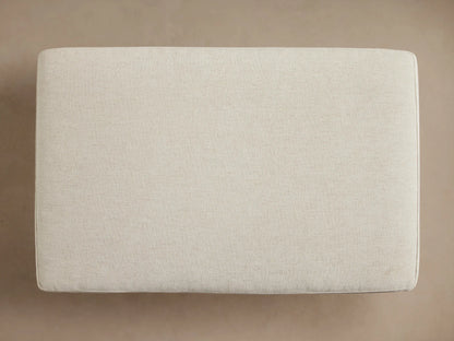 Interior view of an open cream storage ottoman, filled with a folded ribbed taupe blanket and a textured brown throw.