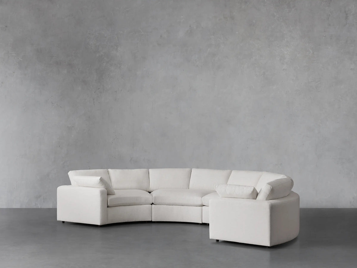 Beale Four-Piece Curved Sectional in off-white fabric, showing its plush seat and back cushions, and low arms. Set against a gray wall.