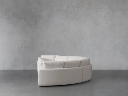 Close-up of the Beale Four-Piece Curved Sectional in white textured fabric. An armrest and back cushion are visible, highlighting its curve.