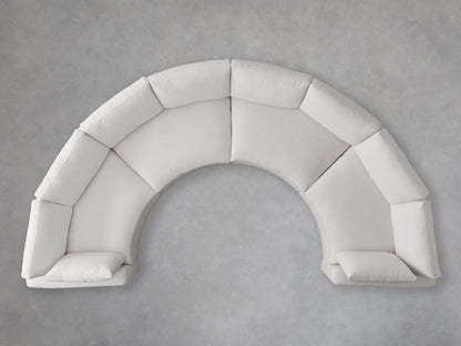 Curved Beale Four-Piece Sectional in light beige fabric, with soft back and seat cushions, on a gray floor against a textured gray wall.