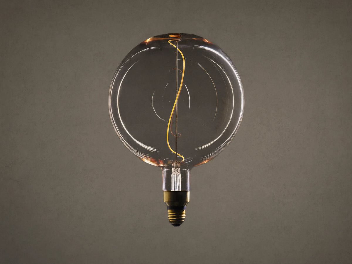 Clear glass globe bulb with amber tint and visible yellow filament inside. E26 base at bottom. Dark background highlighting bulb's design.
